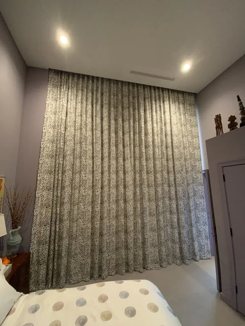 Bedroom with tall, patterned window treatments covering a large window, two ceiling lights, a partial view of a polka-dot bedspread, and decorative items on a cabinet—all combining to highlight thoughtful design and stylish soft furnishings.