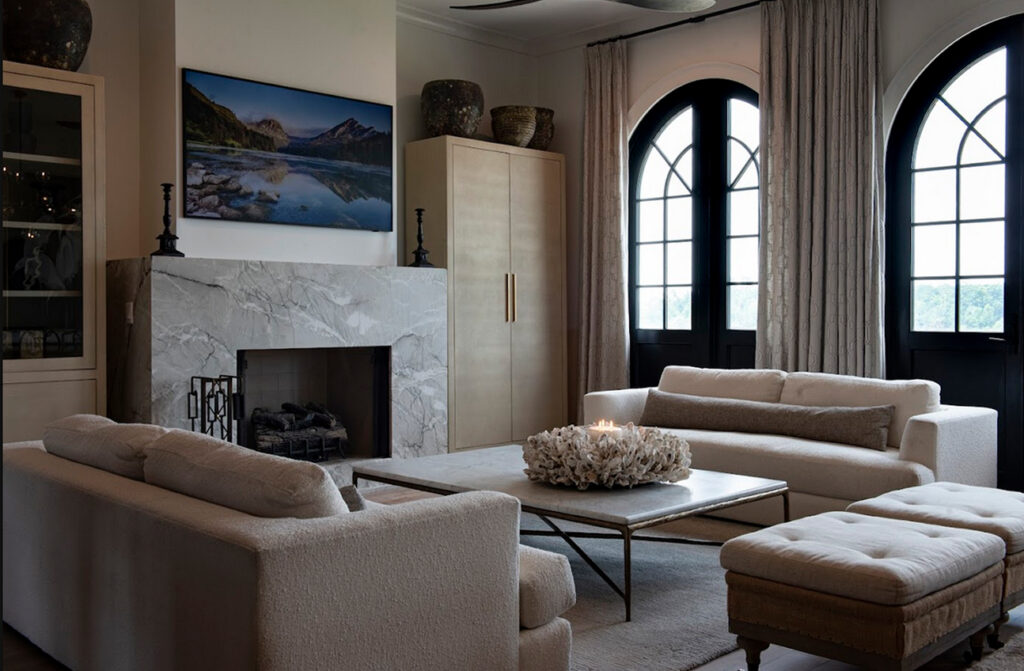 Modern living room with two white sofas, a marble fireplace, a large coffee table, and arched black-framed windows allowing natural light into the space. Soft furnishings enhance the inviting atmosphere, while thoughtfully chosen window treatments add both style and privacy.