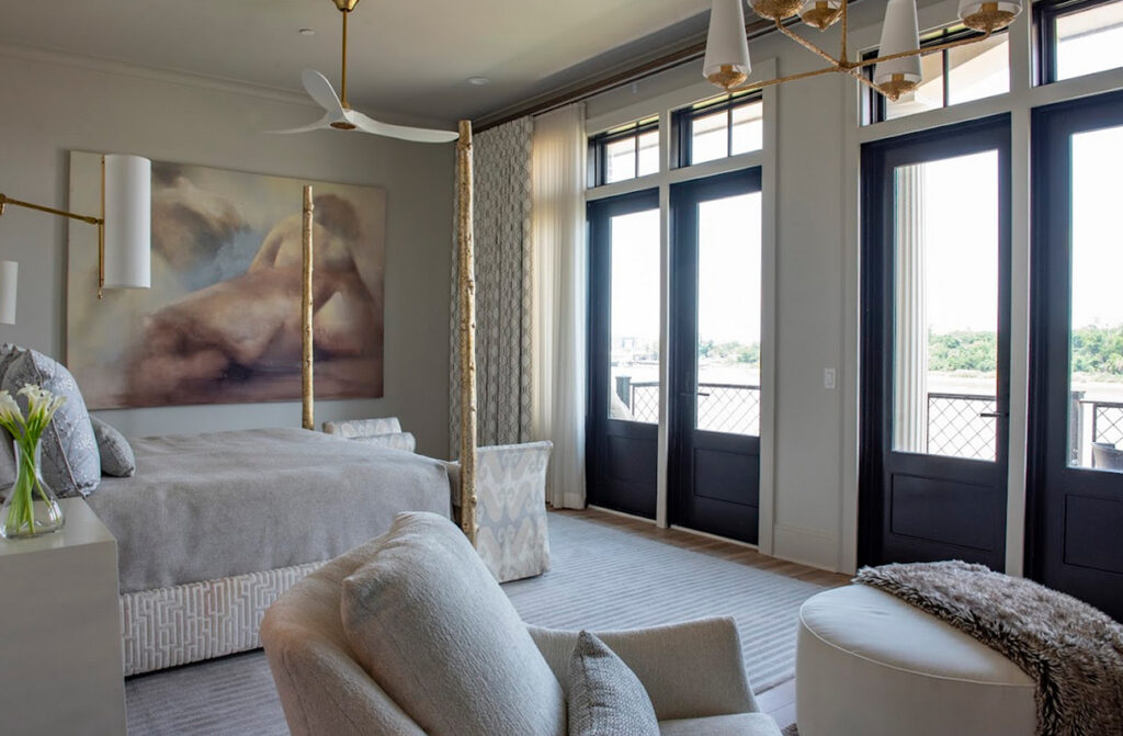 Modern bedroom with large bed, abstract nude painting, seating area, and floor-to-ceiling windows with black frames leading to an outdoor balcony. Soft furnishings and elegant window treatments add warmth and sophistication to the serene space.