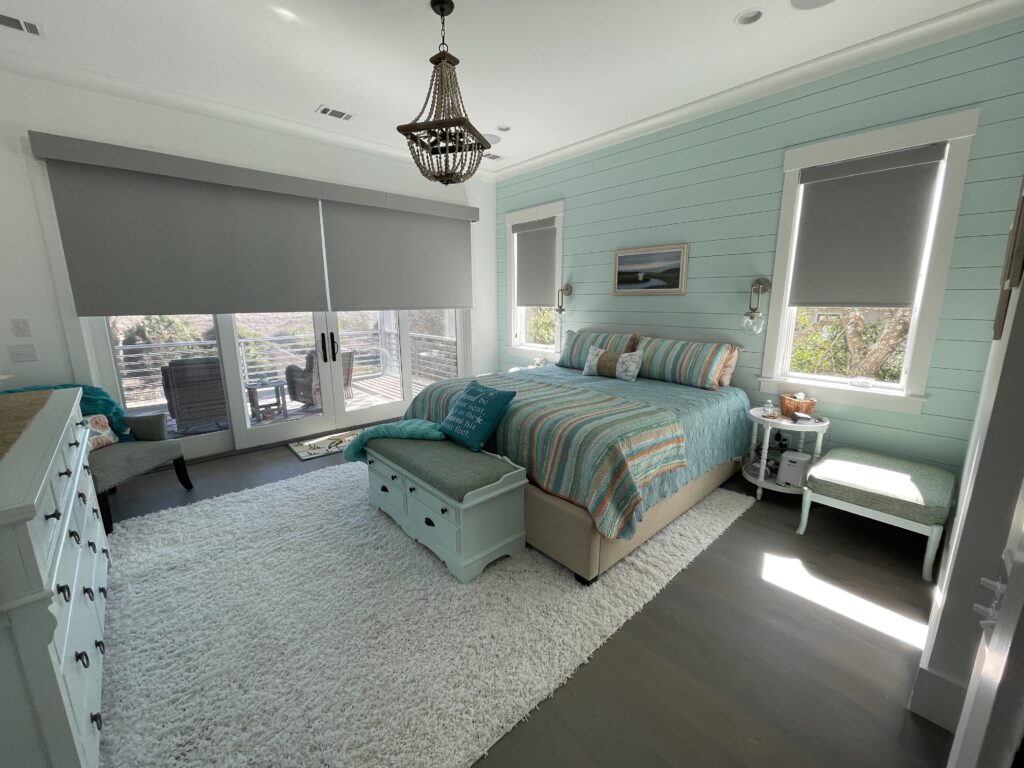 Bedroom with a queen-sized bed, light blue shiplap walls, a white rug, and a storage bench at the foot of the bed.